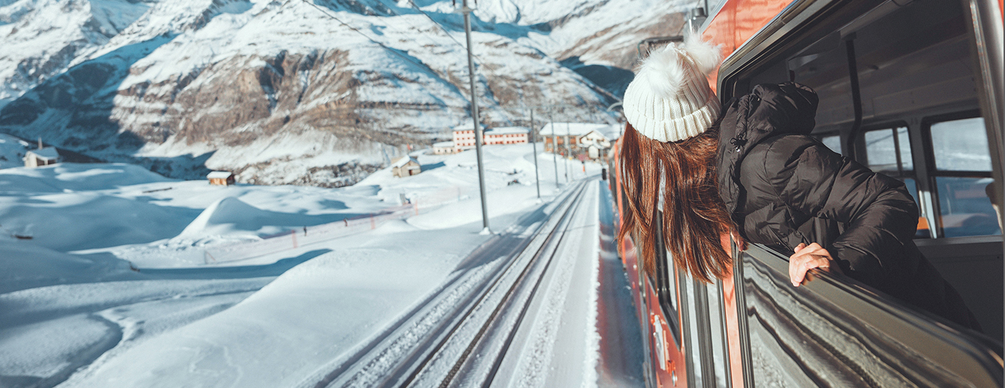 Femme se penchant par la fenêtre d'un train et regardant les montagnes enneigées