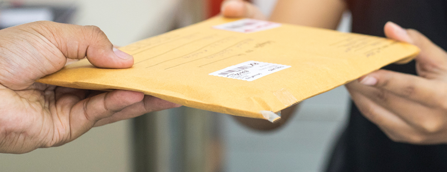 Une main d'homme donne une enveloppe pour envoi par la poste